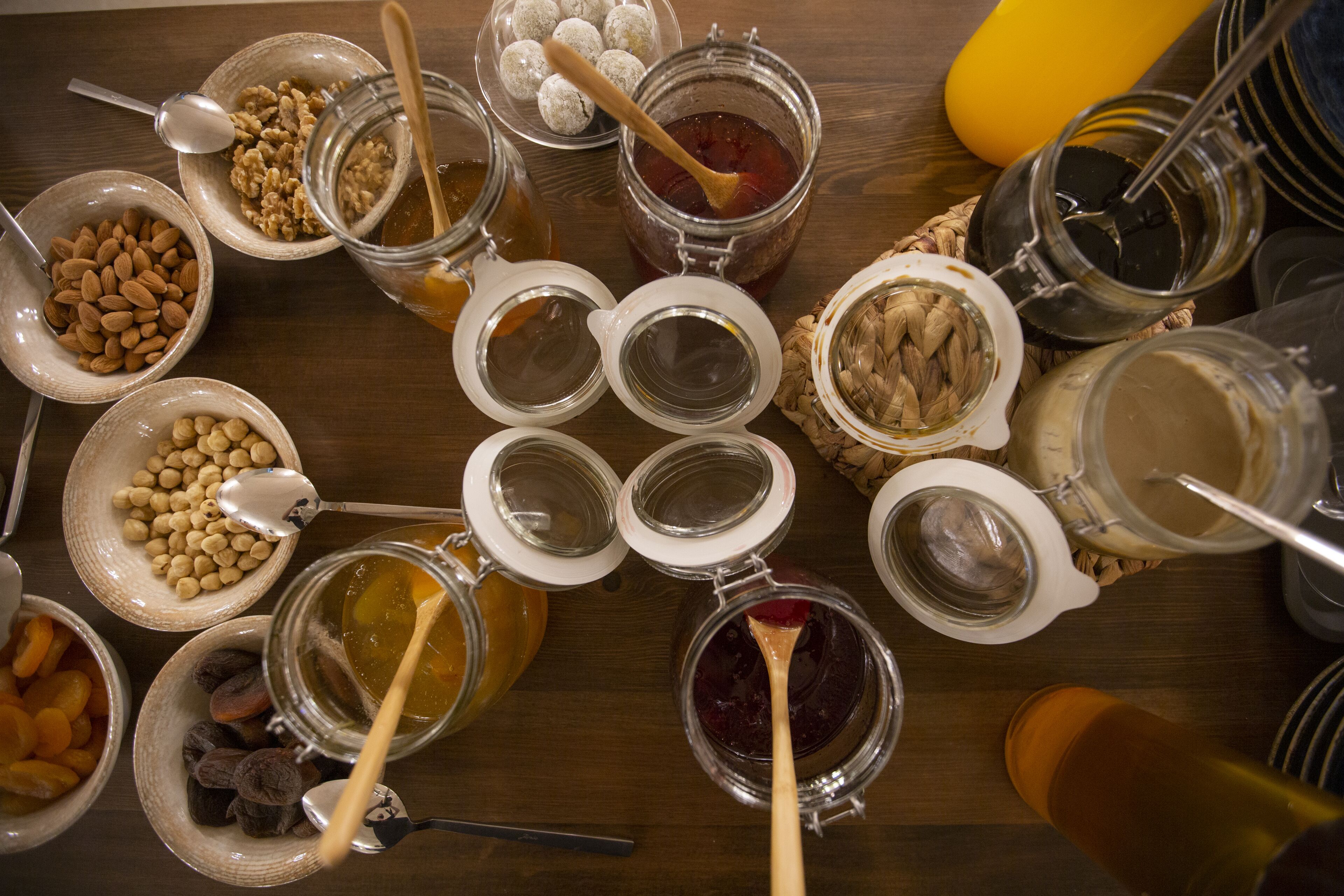 Diversos frascos y recipientes con nueces, semillas y frutas deshidratadas sobre una mesa de madera.