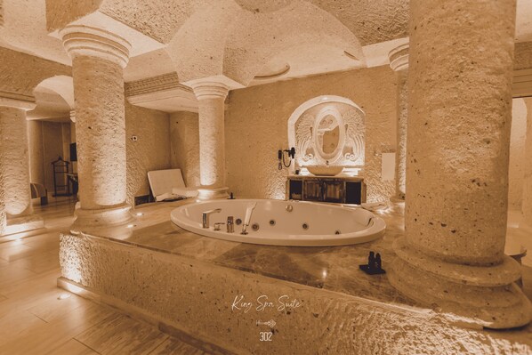 Uma suíte de spa com uma banheira grande, colunas de pedra e um espelho com moldura decorada.