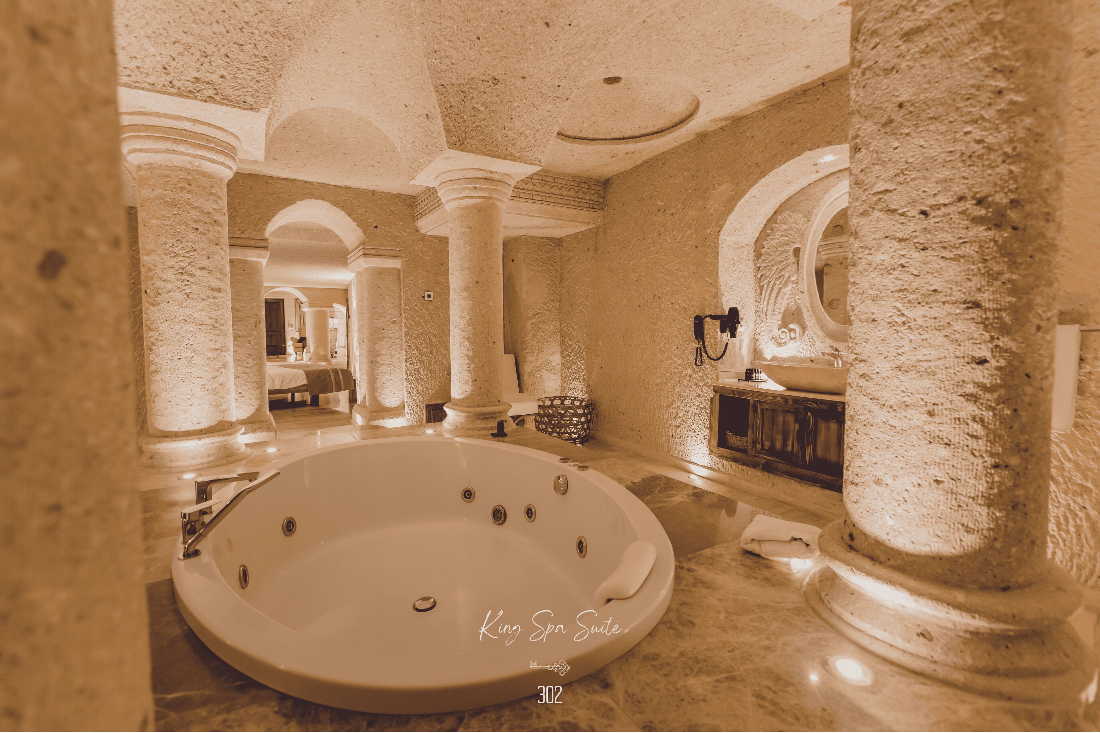 Una suite King Spa con una bañera grande, suelo de mármol y columnas de estilo arquitectónico clásico.