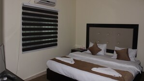 Quarto de hotel com uma cama grande, mesa de cabeceira, ar condicionado fixado na parede e janela com persianas.