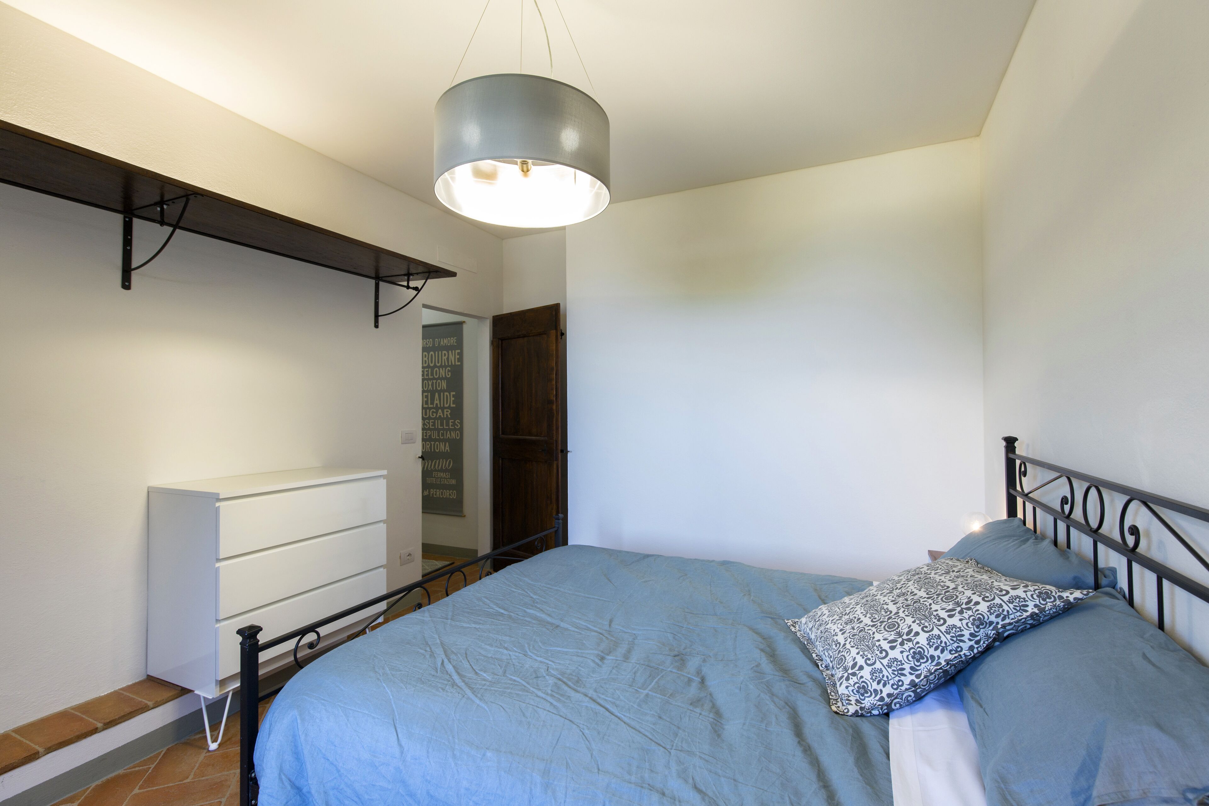 A bedroom with a bed, a bedside table, a wardrobe, and a hanging light fixture.