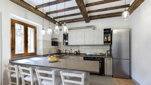Eine Küche mit Kochinsel, weißen Barhocker, einem Edelstahlkühlschrank und Holzbalken an der Decke.