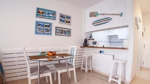 A dining area with a round glass table, white chairs, and a white bench. There are framed pictures on the wall, a microwave, and a small kitchen counter. - Las Vistas Beach 2 minutes to the Beach (Arona)