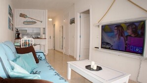 A living room with a sofa, a coffee table, and a television displaying a show. There is a kitchen area in the background. - Las Vistas Beach 2 minutes to the Beach (Arona)