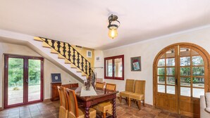 A dining area with a wooden table and chairs, a staircase with a black and white railing, and a large arched window with a view of greenery.