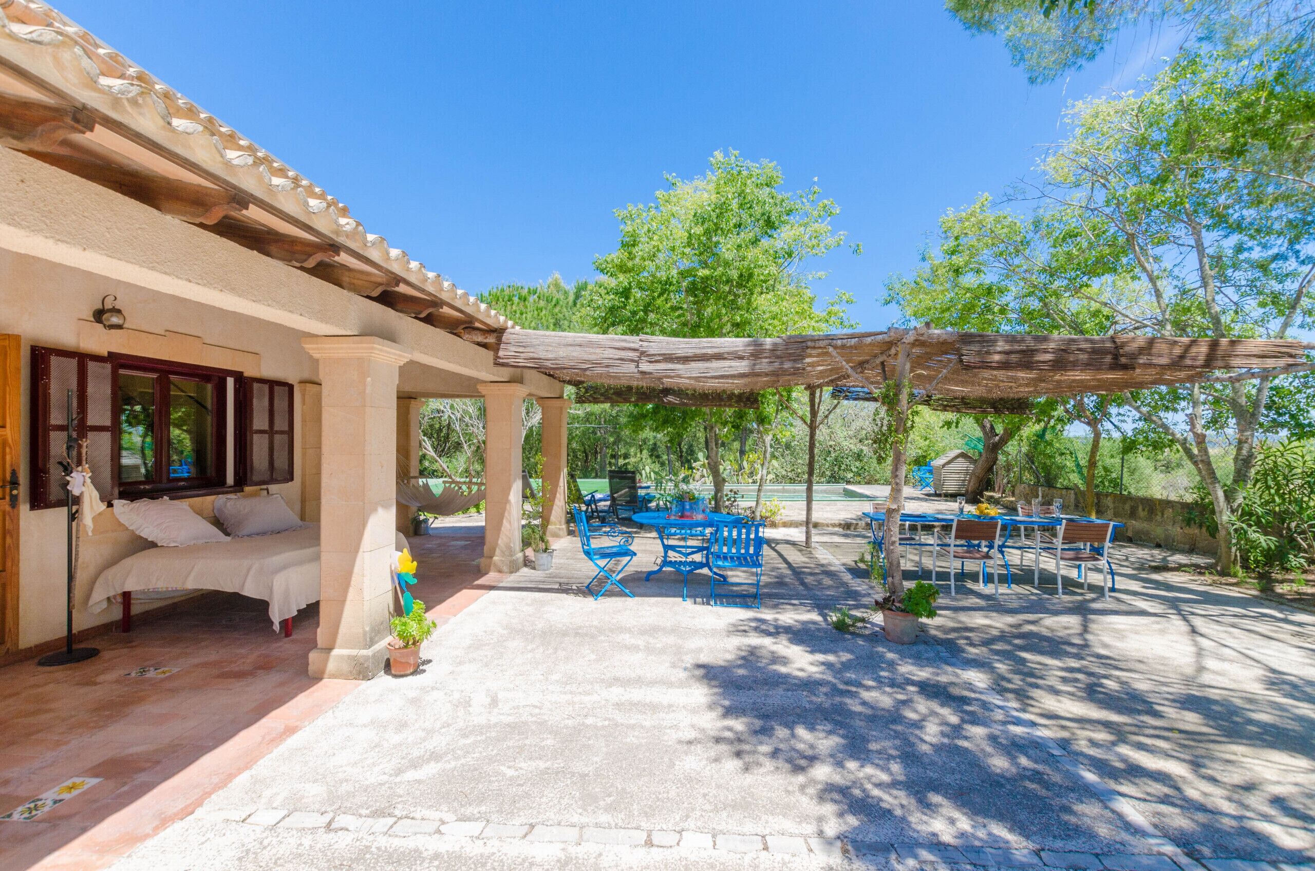 Un área de estar al aire libre cubierta con mesa y sillas, un sofá y una pérgola que ofrece sombra.