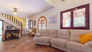A living room with a beige sectional sofa, a wooden staircase, and a dining area with a table and chairs.