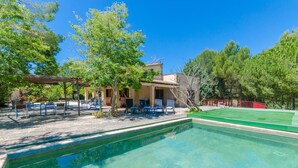 A pool area with clear water, surrounded by trees and a building with a pergola.