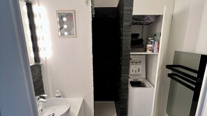Cozinha moderna com bancada branca, pia e forno embutido. Possui painel de parede preto e uma pequena planta na parede.