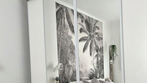 Quarto com cama, mesa de cabeceira, espelho e um mural tropical na parede.