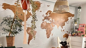 Uma sala de estar com um mural de mapa mundi, sofá verde, baú de madeira e plantas penduradas.