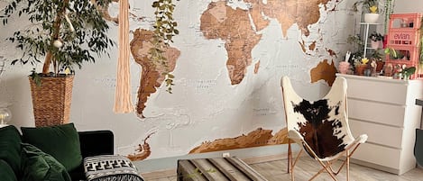 A living room with a world map mural, green sofa, wooden chest, and hanging plants.