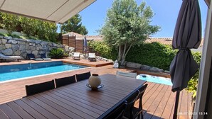 Un patio in legno con piscina, lettini e un muro in pietra.