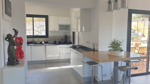 Una cucina moderna con mobili bianchi, un'isola in legno e un'ampia porta scorrevole in vetro che si apre su un patio esterno.