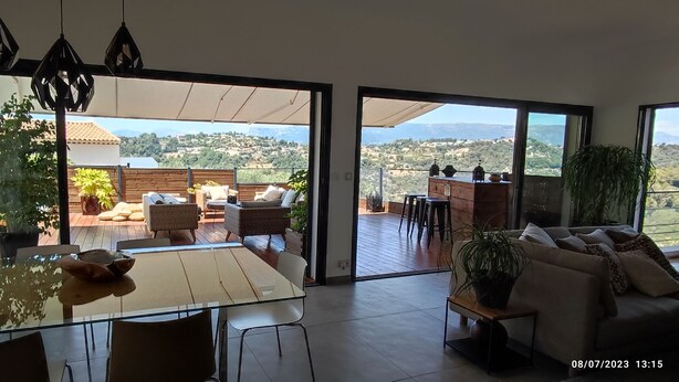 Un'ampia zona giorno con una grande porta vetrata che si apre su un patio esterno. All'interno, si trova un tavolo da pranzo con sedie, un divano e un tavolino da caffè. L'ambiente presenta un design moderno, con una grande finestra che offre vista sull'esterno.
