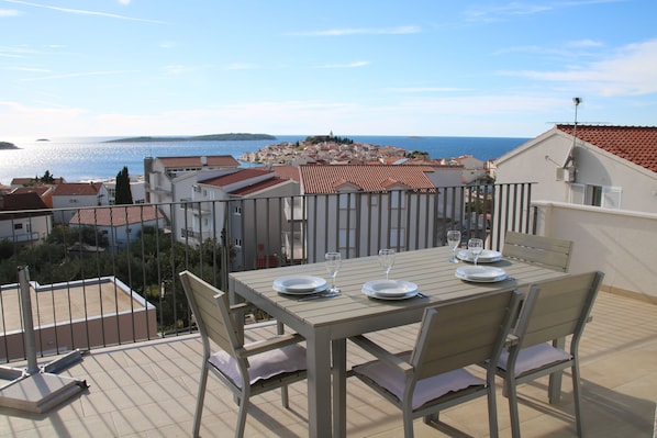 A terrace with a table set for two, overlooking a coastal town.