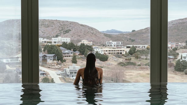 Una persona en una piscina con vistas a casas y colinas al fondo.