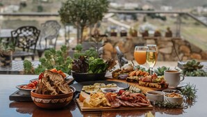 Una mesa dispuesta con una variedad de alimentos y bebidas, como pan, queso, carnes y una ensalada, con una vista panorámica de fondo.