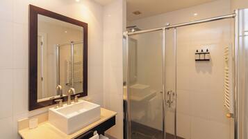 Een moderne badkamer met een grote spiegel, een witte wastafel en een douche met glazen wanden.