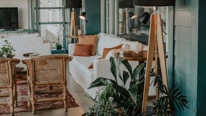Una sala de estar moderna con un sofá, sillas de mimbre, una mesa de centro y plantas en macetas.