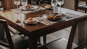 Comedor con una mesa de madera preparada para dos personas, con platos de comida y copas de vino blanco.