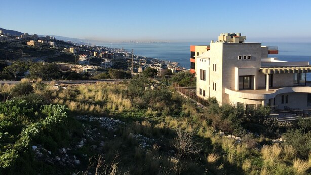 Zona residencial costera con edificios modernos, vista despejada del mar y un paisaje montañoso.
