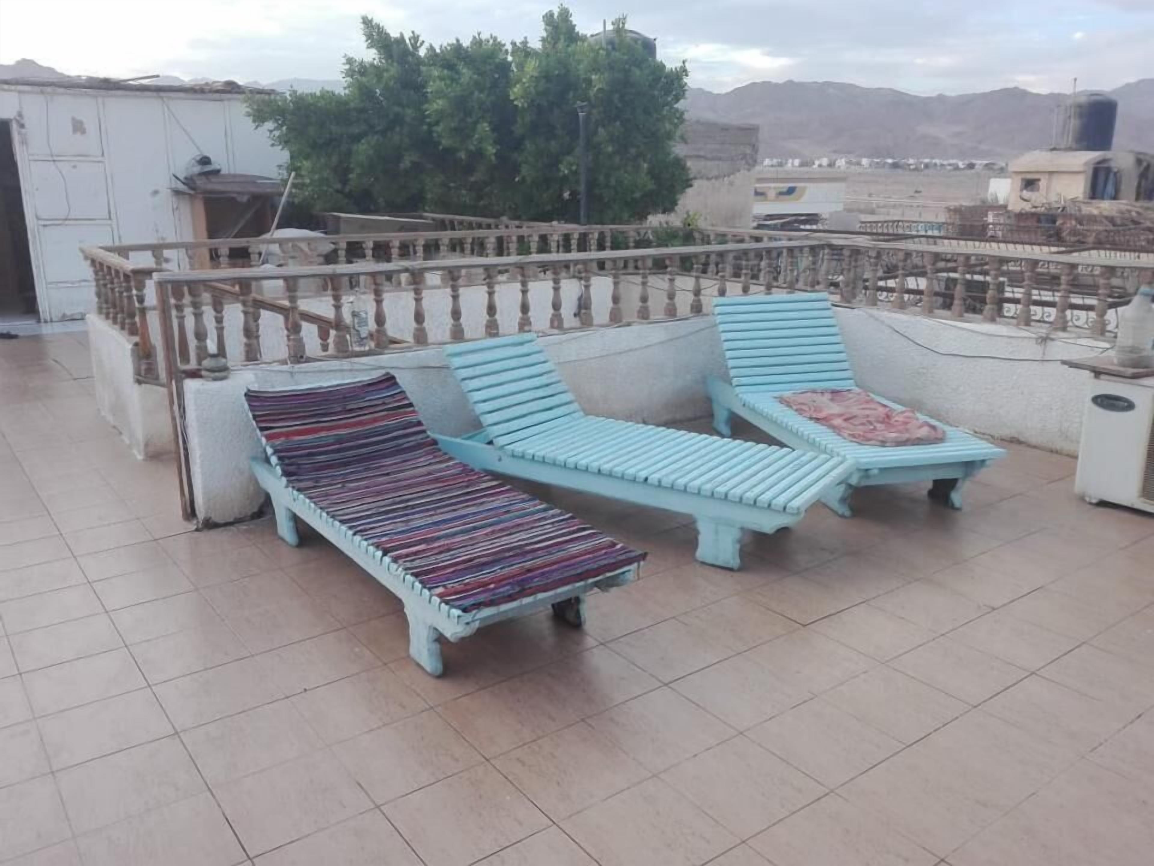 Une terrasse sur le toit, avec deux fauteuils de couleur bleu clair et un coussin à motifs, une rambarde en bois et une vue sur un paysage montagneux.