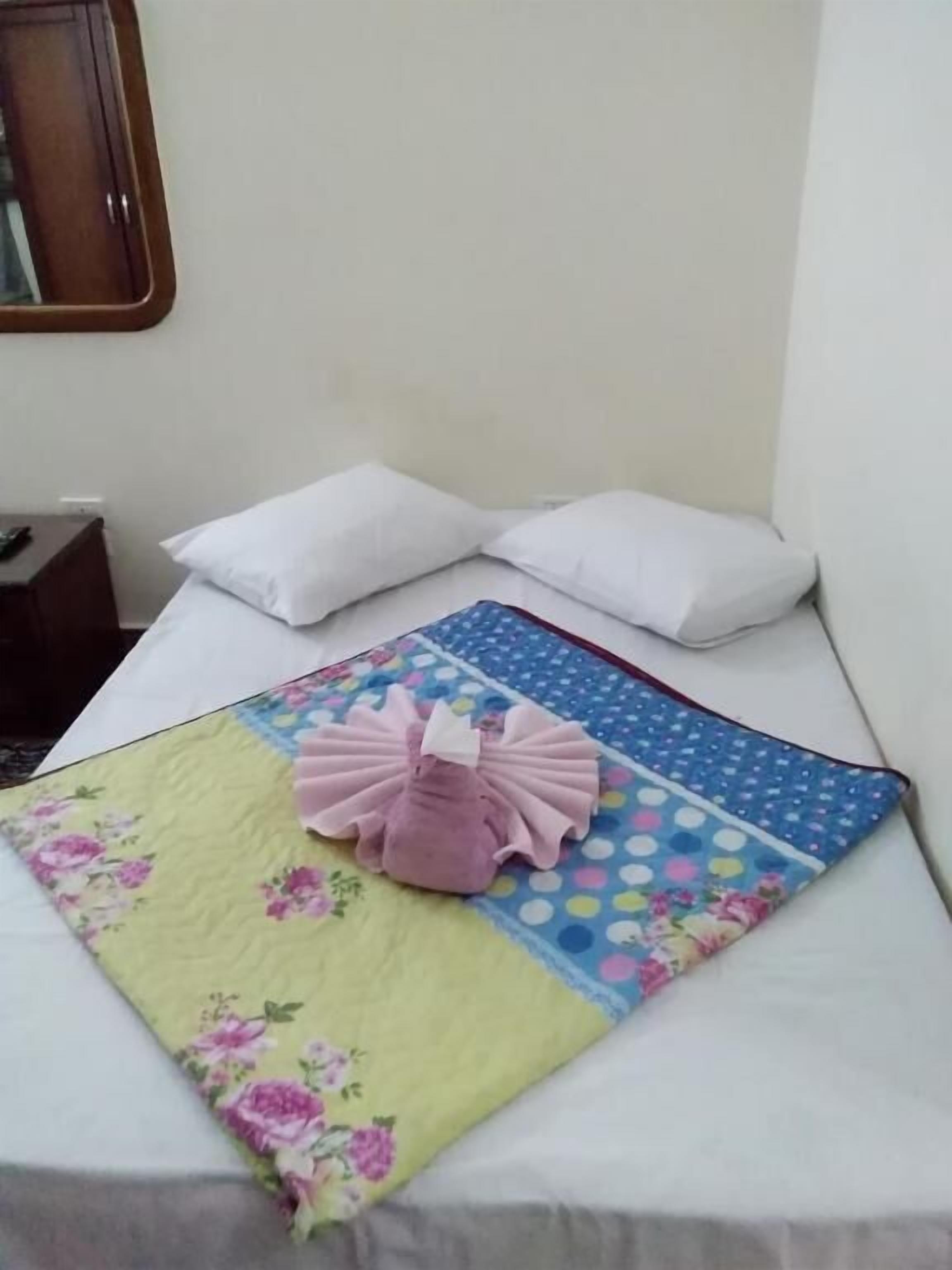 A bed with a floral-patterned blanket, two white pillows, and a decorative pink item on the bed.
