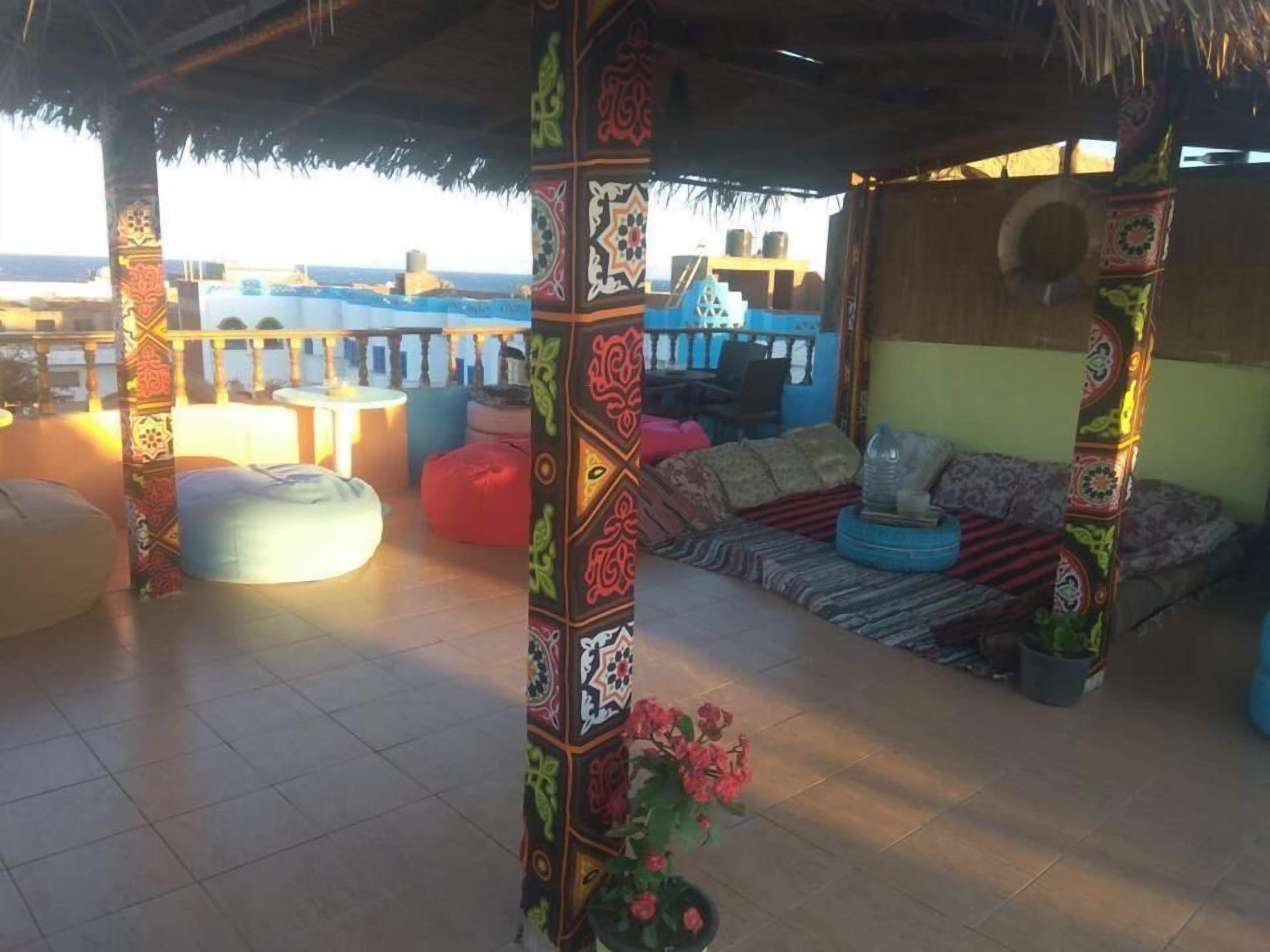 Un espace extérieur abrité, doté de piliers aux motifs et couleurs vives, d’un toit de chaume et offrant une vue sur la mer.