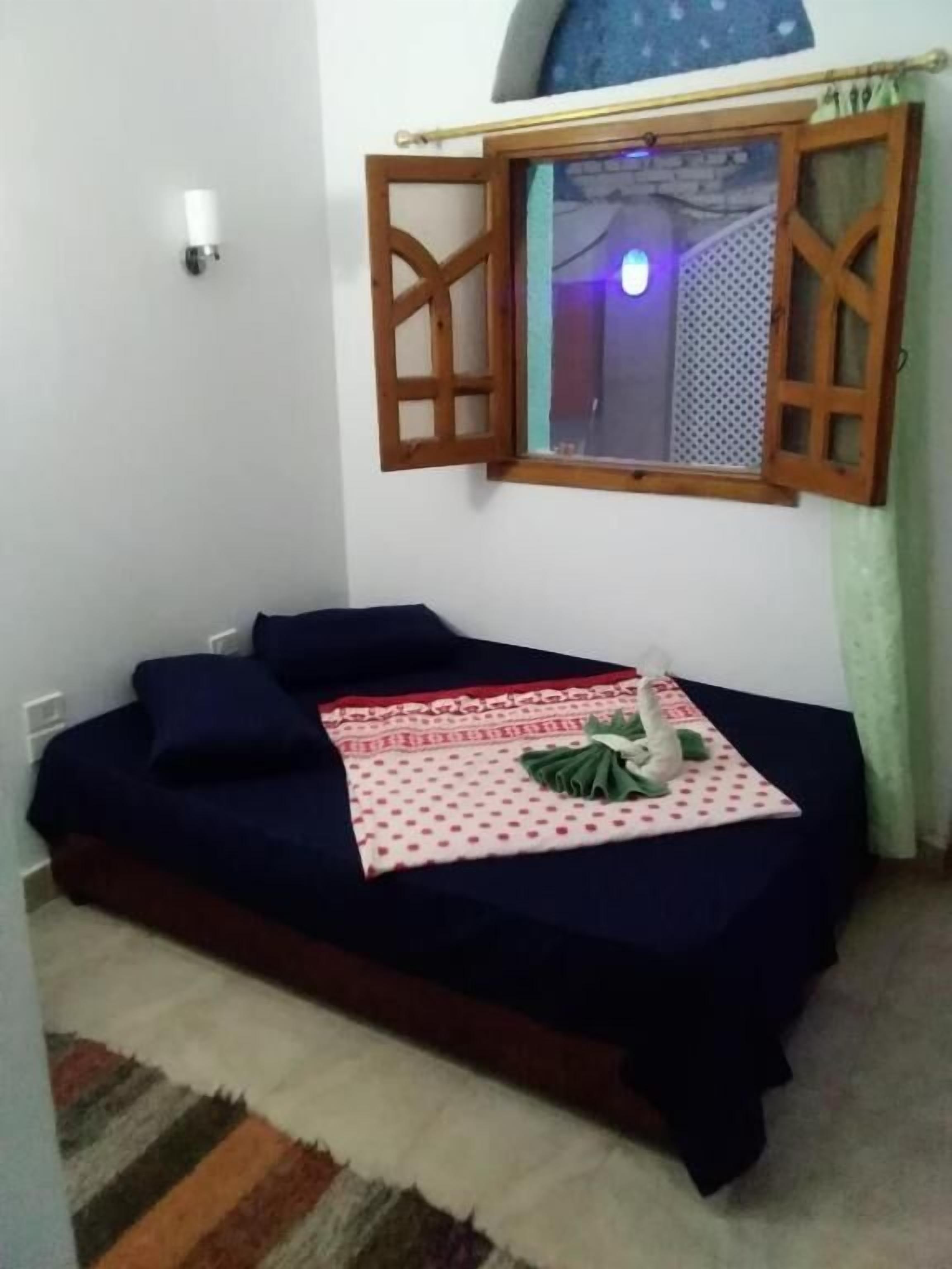 A small, cozy room with a single bed, a window with wooden shutters, and a wall-mounted light fixture.
