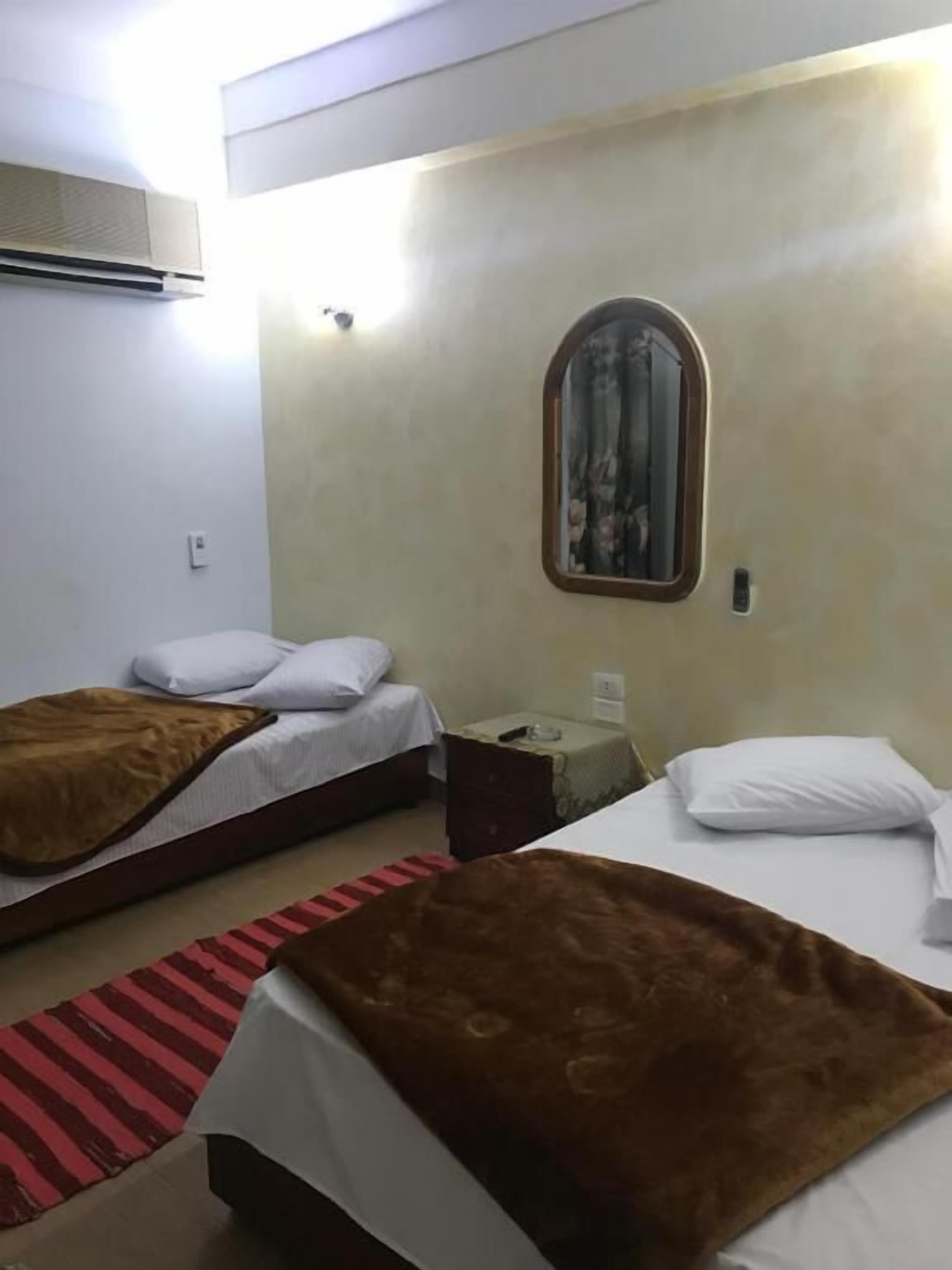 A hotel room with two beds, a mirror, a small table, and a red striped rug.