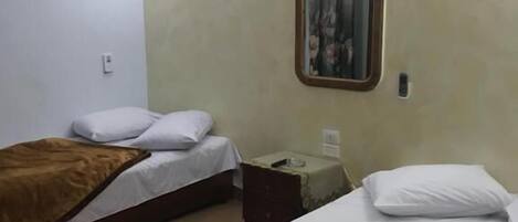 A hotel room with two beds, a mirror, a small table, and a red striped rug.