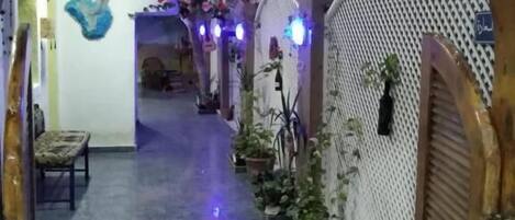 Un pasillo con un arco de madera, decorado con flores y plantas de papel colgantes, que conduce a una habitación con suelo estampado y una cama.