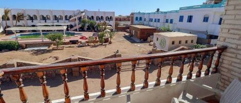 Un balcón con vista a un patio que cuenta con una piscina, palmeras y edificios tradicionales.