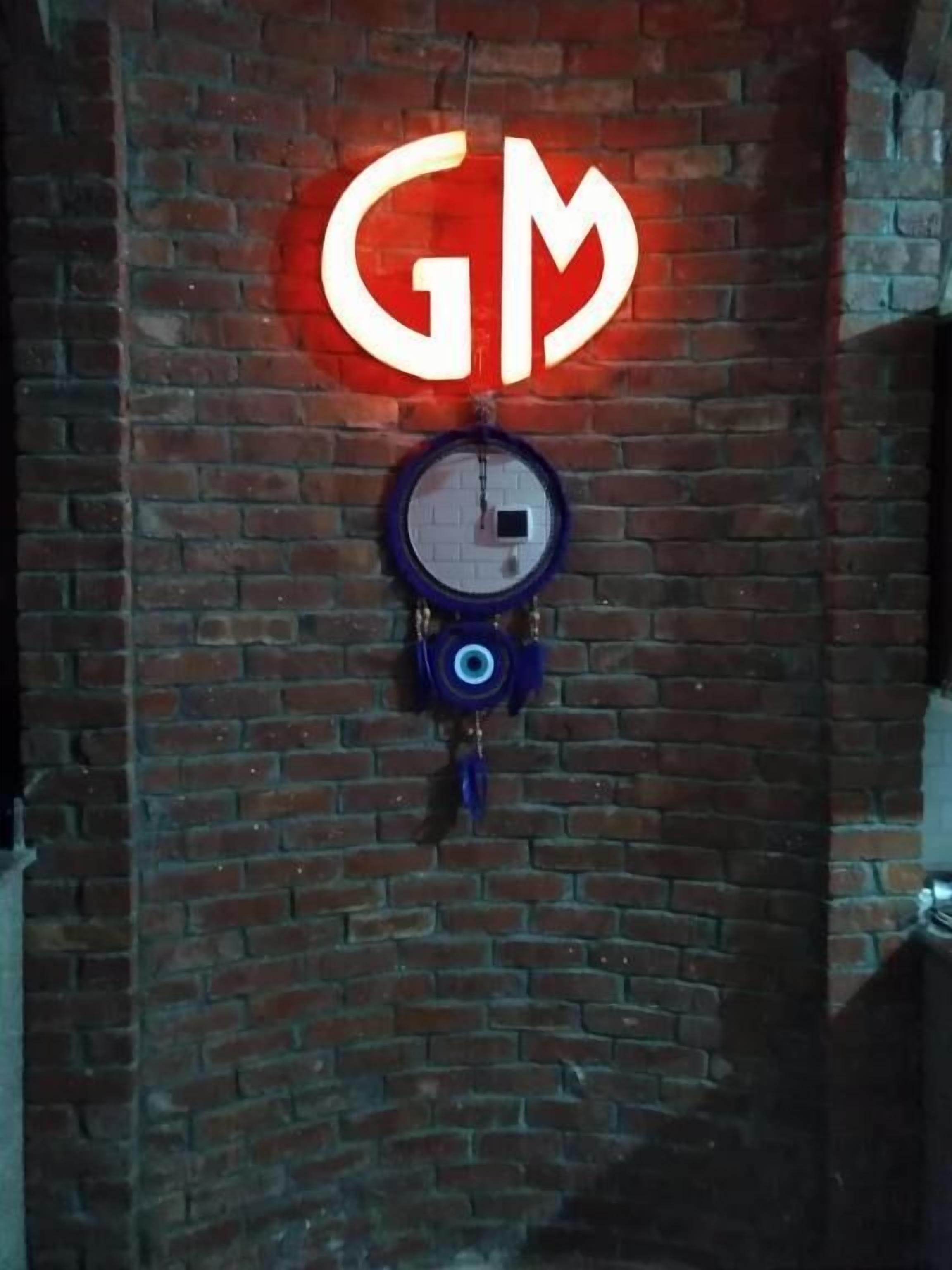 A neon GM sign and a clock on a brick wall.