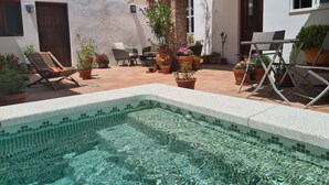 A pool area with tiled flooring, lounge chairs, potted plants, and a small table.