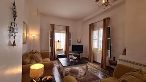 A living room with a sofa, a coffee table, a TV, and a chandelier.