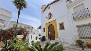 A narrow street with white buildings, a yellow door, and a palm tree.