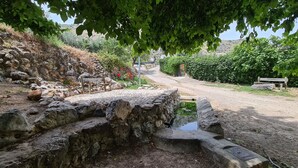A rustic stone bridge over a small stream, surrounded by greenery and a bench.