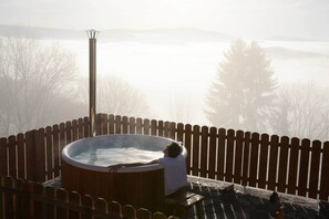 Un bain à remous sur une terrasse en bois, entouré d’une clôture en bois, de nombreux arbres et d’un paysage brumeux.