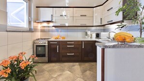 A modern kitchen with a built-in oven, a microwave, and a sink. There is a window providing natural light, and a plant is visible on the countertop. - Holiday apartments Carmen / Carmen Garden (Pula)