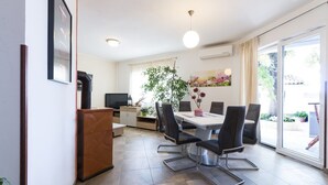 A modern kitchen with a dining area, including a table and chairs, a TV, and a plant. - Holiday apartments Carmen / Carmen Garden (Pula)