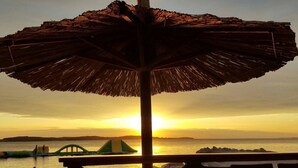 A beachside view with a thatched umbrella, chairs, and a sunset over the water. - Holiday apartments Carmen / Carmen Garden (Pula)