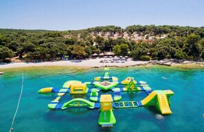 Luchtbeeld van een strand met opblaasbare waterattracties in de zee en een kustplaats op de achtergrond.