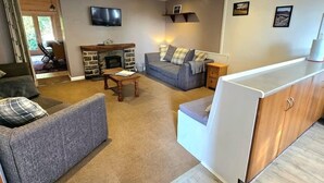 Una sala de estar con sofá, mesa de centro, chimenea, televisor y una zona de cocina con encimera y armarios.