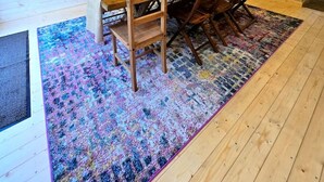 Un comedor con una mesa y sillas de madera, un tapete colorido y una lámpara colgante.