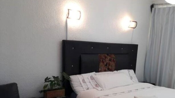 Quarto de hotel bem organizado, com uma cama, um pequeno sofá e uma mesa de cabeceira com abajur.