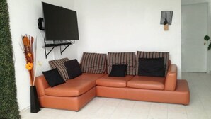 Uma sala de estar moderna com um sofá seccional, uma TV de tela plana na parede e uma pequena planta ao lado.