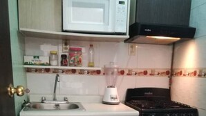 Cozinha compacta com micro-ondas, fogão, pia e liquidificador na bancada.