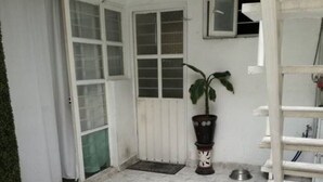 Um quarto com piso de azulejos, uma planta em vaso, uma tigela de metal e uma estante branca.